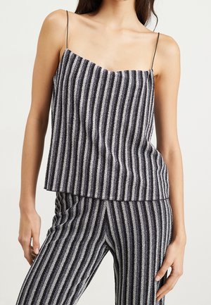 Mujer con top sin mangas de rayas verticales blancas y negras con tirantes finos y pantalones a juego frente a un fondo liso.