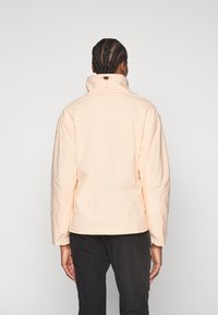 Veste de couleur pêche clair avec un col montant, des poignets élastiques et une texture lisse et gonflée. Design simple sans matériel visible ni motifs.