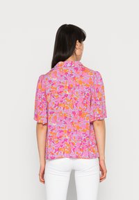 Krátký rukáv blouse v živé růžové barvě s květinovým potiskem, který obsahuje oranžové a modré akcenty. Lehká, hladká tkanina s uvolněným střihem.