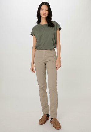 T-shirt a maniche corte verde oliva abbinato a pantaloni beige aderenti e mocassini marroni. Tessuto liscio, design casual e colori neutri.