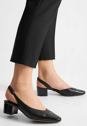 Czarne sandały na obcasie typu slingback z pointed toe i błyszczącym lakierowanym czubkiem. Charakteryzują się masywnym obcasem oraz regulowanym paskiem wokół kostki, wykonane z gładkiej skóry.
