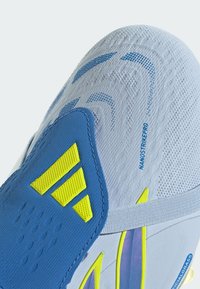 Gros plan sur une chaussure de football blanc et bleu avec le logo Adidas jaune, une tige texturée et le texte « NANOSTRIKEPRO » sur la zone des orteils.