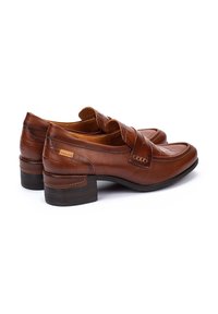 Mocassins en cuir marron avec un petit talon carré, présentant un design texturé et une sangle sur le dessus, des coutures détaillées et un logo discret.