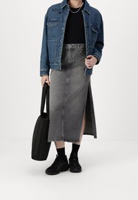 Chaqueta de mezclilla azul con bolsillos frontales, combinada con una falda de mezclilla gris de cintura alta con una abertura lateral, zapatillas negras y un bolso negro.