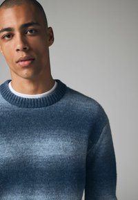 Blauer Gradient-Pullover mit einem gerippten Rundhalsausschnitt und weicher Textur, der von dunkelblau nach hellblau übergeht.