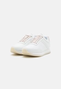 Baskets blanches en matériau lisse avec des lacets roses, un logo discret sur le côté et une semelle en caoutchouc texturée de couleur claire.