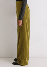 Wijduitlopende corduroy broek in olijfgroen met verticale ribbelstructuur. Hooggewerkte stijl, gecombineerd met zwarte schoenen voor contrast.