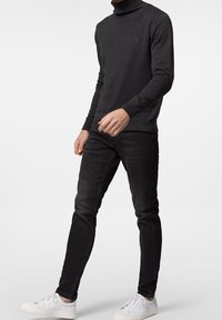 Mörkgrå polotröja med kroppsnära passform, kombinerad med smala svarta jeans och vita sneakers, som visar upp en minimalistisk stil.