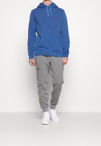 Sudadera de algodón azul con un bolsillo frontal y dobladillo acanalado, combinada con joggers cargo grises con bolsillos laterales, llevada con zapatillas blancas.