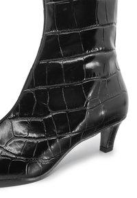 Stivaletto nero realizzato in ecopelle lucida a effetto coccodrillo; presenta una punta affusolata e un tacco triangolare basso. Motivo testurizzato visibile.