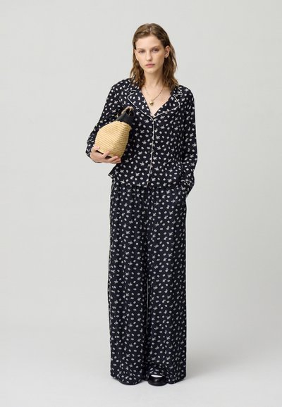Set di pigiama nero con fiori, caratterizzato da piccoli fiori bianchi, maniche lunghe e pantaloni larghi, con piping chiaro a contrasto; da abbinare a una borsa intrecciata.