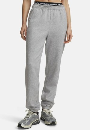 Persoon draagt lichtgrijze joggingbroek met elastische boorden en een zwarte tailleband met het merk Under Armour, gecombineerd met grijze en witte hardloopschoenen.