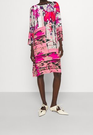 Robe à motif floral aux couleurs rose, blanc et gris, avec des manches trois-quarts et une coupe ample. Associée à des ballerines blanches à bout pointu.