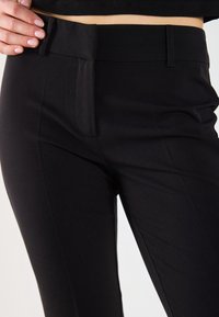 Black tailored trousers featuring a smooth texture, slim fit, subtle front pleats, and belt loops for adjustable fit.