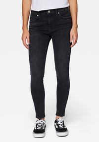 Jeans skinny negros de mezclilla, con cinco bolsillos, cierre de botón y detalles de costura sutiles. Llevados con zapatillas negras.