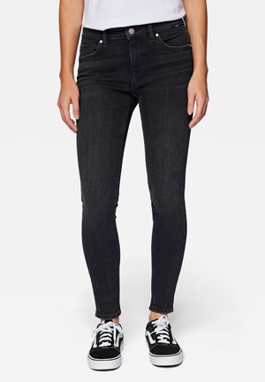 Jeans skinny negros de mezclilla, con cinco bolsillos, cierre de botón y detalles de costura sutiles. Llevados con zapatillas negras.