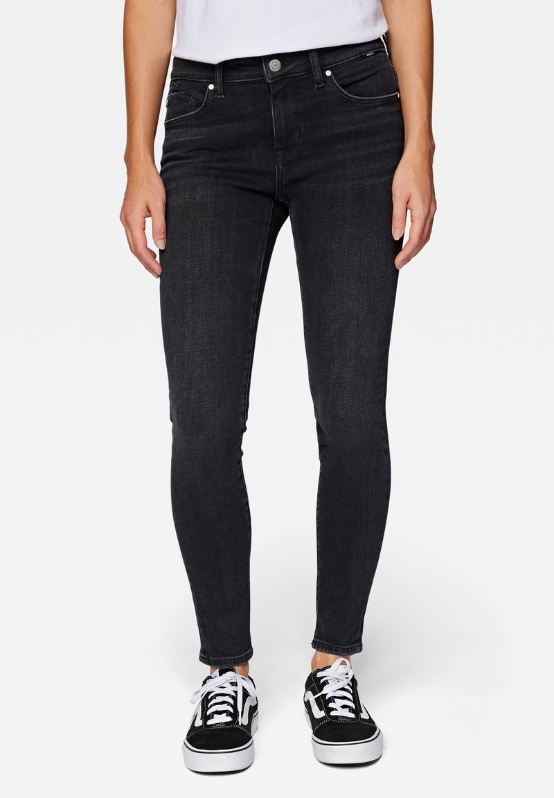 Jeans skinny negros de mezclilla, con cinco bolsillos, cierre de botón y detalles de costura sutiles. Llevados con zapatillas negras.