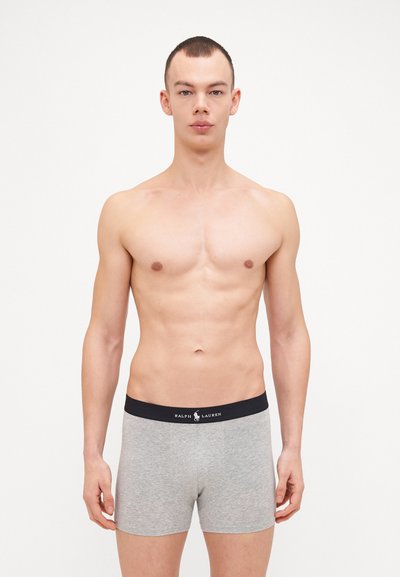 Sivi bombažasti bokserici z črnim pasom, na katerem je napis "Ralph Lauren". Tkanina izgleda gladka in ima prilagojeno obliko.