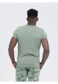 Oliwkowa koszulka z krótkim rękawem i okrągłym dekoltem, w połączeniu z jas green spodniami w liście. Materiał wydaje się gładki i miękki.