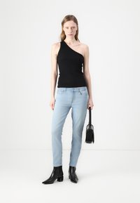 Black one-shoulder top, light blue slim-fit jeans, and black heeled boots. The model holds a small black handbag. Minimalist design, neutral colors.