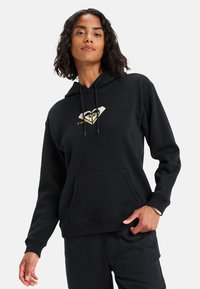 Sudadera negra hecha de un material suave, con un bolsillo frontal, capucha ajustable con cordón y un diseño de logo dorado en el pecho.