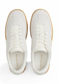 Sneakers bianchi in pelle liscia, con un design perforato, punta arrotondata e suola in gomma di tonalità marrone chiaro. I lacci sono posizionati al centro.