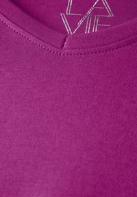Fuchsia T-shirt met een V-hals ontwerp, met een gladde textuur en een metallic zilveren logo detail bij de hals.