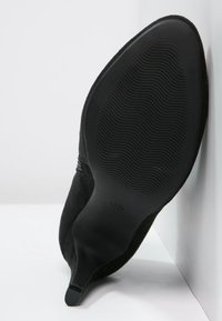 Scarpa con tacco alto in suede nero con un design curvo e liscio e una suola in gomma testurizzata con scanalature per una migliore aderenza.