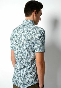 Korte mouwen shirt van lichte stof, met een lichtblauwe achtergrond en donkergroene en grijze bladerenpatronen, en een gestructureerde kraag.