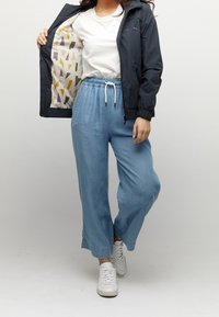 Lekka granatowa kurtka z elastycznymi mankietami, biały t-shirt i luźne niebieskie culotte. Buty to białe trampki, a wnętrze kurtki zdobi geometryczny wzór.