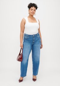 White square-neck bodysuit, light blue high-waisted jeans, burgundy patent handbag, matching heels, curly hair with gold hoop earrings.