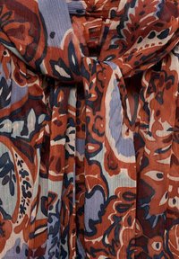 Écharpe multicolore aux motifs floraux et abstraits en rouille, bleu et crème. Fabriquée en tissu léger et texturé, attachée en boucle souple.