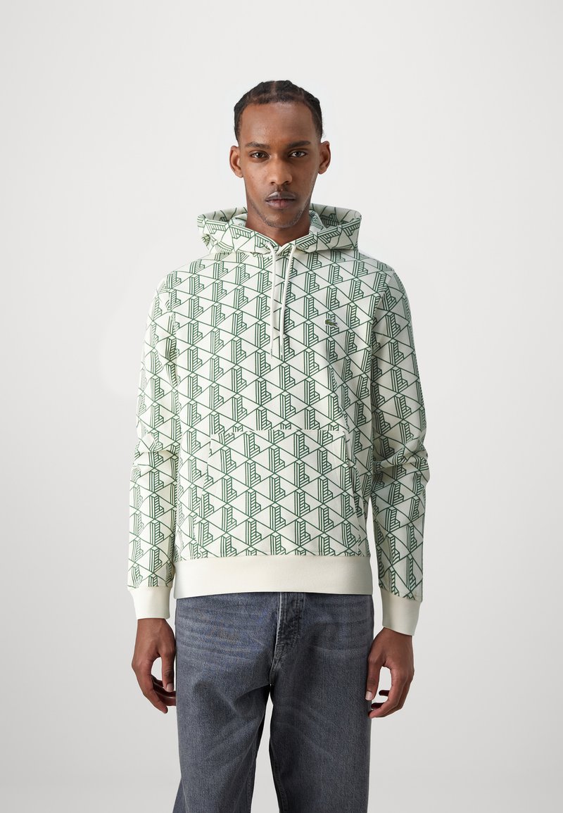 Felpa con cappuccio verde chiaro con un motivo geometrico, realizzata in tessuto morbido. Presenta una tasca frontale e polsini a costine. Indossata con jeans in denim scuro.