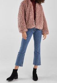 Rosa fluffig fuskpälskort jacka över en vinröd topp, ihop med ljusblå raka jeans och svarta mocka ankelstövlar.