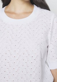 Top in cotone bianco con un design testurizzato di motivi foglia ritagliati, scollo a costine e maniche corte.