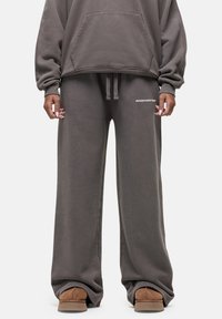 Oversized grijze hoodie met een voorzak, gecombineerd met ruime grijze sweatpants met een wit logo. Zachte stoftextuur, casual ontwerp.