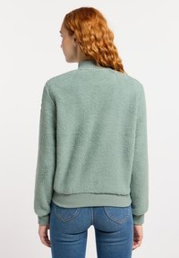 Fuzzy groene fleece jack met een geribde kraag en mouwen, met een eenvoudig ontwerp. De stof heeft een zachte, gestructureerde kwaliteit.
