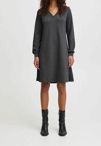 Grå långärmad klänning med V-ringning, med en avslappnad passform och slät textur. Bärs med svarta ankelstövlar.