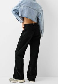 Cropped light blue denim jacket, paired with high-waisted black wide-leg jeans. Jeans feature back pockets and a textured finish.