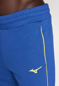 Blue stretch joggers with a yellow stripe along the side, featuring an elastic waistband and a small logo in yellow on the thigh.