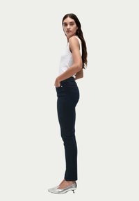 Mörkblå skinny jeans i denim, med fem fickor och subtila sömmar, kombinerade med en vit ärmlös topp och silverfärgade skor.