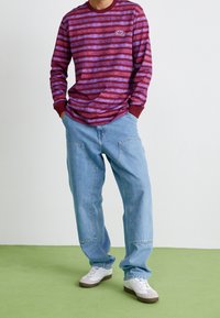 Långärmad skjorta i vinröd med ränder, med rund halsringning, tillsammans med ljusblå, löst sittande jeans och vita sneakers.