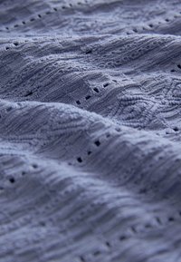 Gros plan d’un tissu bleu doux et texturé avec des motifs tricotés complexes et de petits détails ajourés sur une surface légèrement froissée.