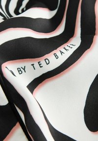 Jedwabny szalik z falistym wzorem w czerni i bieli z różowymi akcentami, przedstawiający tekst "BY TED BAKER" w eleganckiej czcionce.