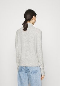 Pull gris clair avec un col montant et des manches longues, confectionné dans un matériau doux. Il présente une coupe décontractée et un ourlet côtelé. Jean en denim visible en dessous.