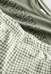 Olive green t-shirt with "OPENHAGE" text above a light green and white gingham-patterned bottom, featuring an elastic waistband.