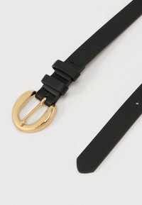 Μαύρη δερμάτινη ζώνη με οβάλ χρυσή πόρπη, με λεία υφή και κλασικό σχέδιο. Ρυθμιζόμενη με πολλαπλές τρύπες για στερέωση.