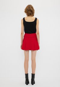 Top sin mangas negro combinado con una minifalda plisada roja. La falda cuenta con un detalle de cinturón y una cremallera en la parte posterior. Botines negros de tacón.