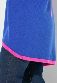 Maglione blu a maglia con orlo a coste rosa, caratterizzato da una vestibilità comoda e una morbida consistenza, abbinato a un paio di jeans in denim blu scuro.