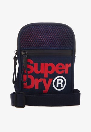 Granatowa torba na ramię z czerwonym napisem „Super Dry®”, górna część z siateczki, czarny zamek błyskawiczny, podwójne czarne suwaki oraz regulowany pasek.